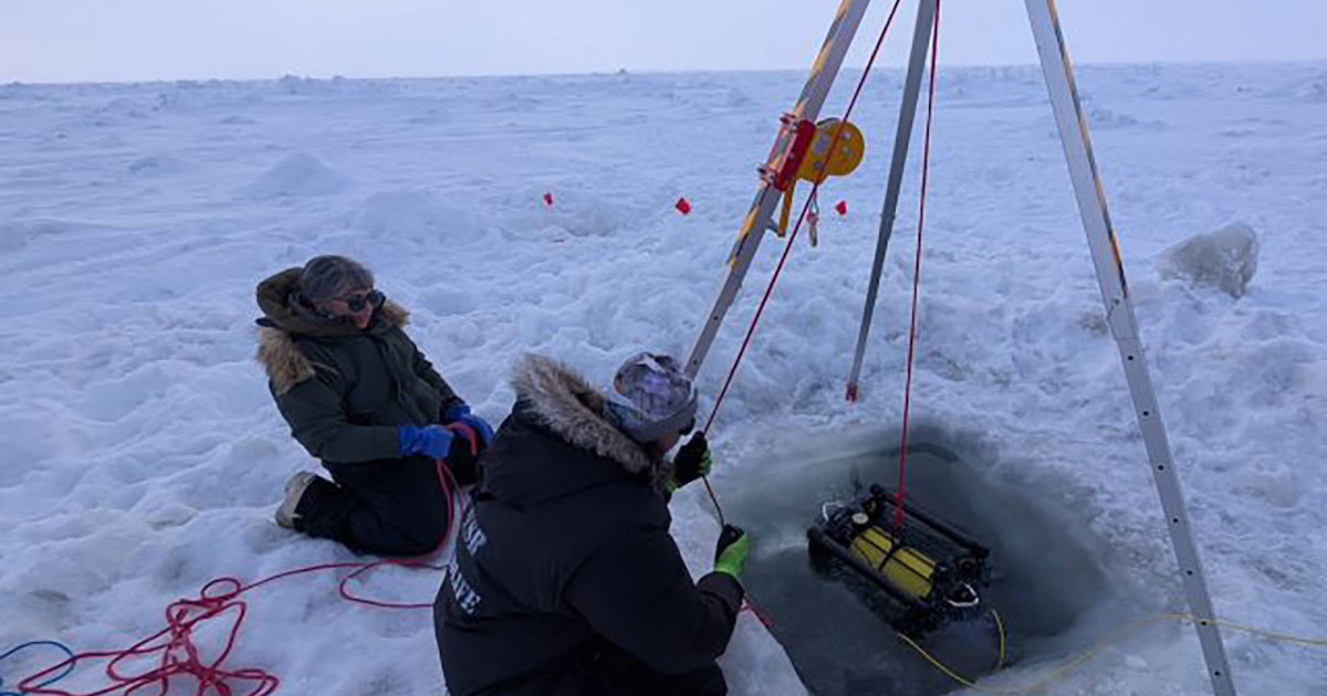 Two scientists retrieve a robotic submersible after deployment under the ice.