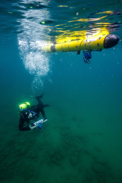 At the Great Lakes Research, David Whelihan swims with a prototype "tube-let," a tube-shaped tablet instrumented with position and velocity sensors, alongside an AUV equipped with a custom optical-acoustic sensor payload.