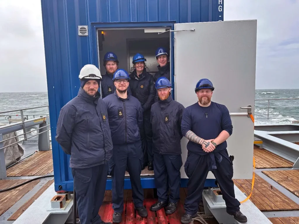 The team poses in front of their command pod on RFA Proteus.